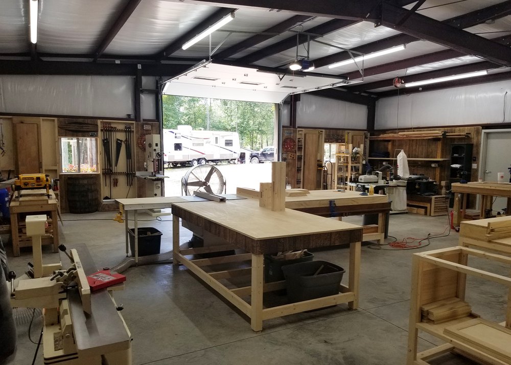 Working woodshop interior inside a red-iron rigid-frame steel building — a workshop configuration.