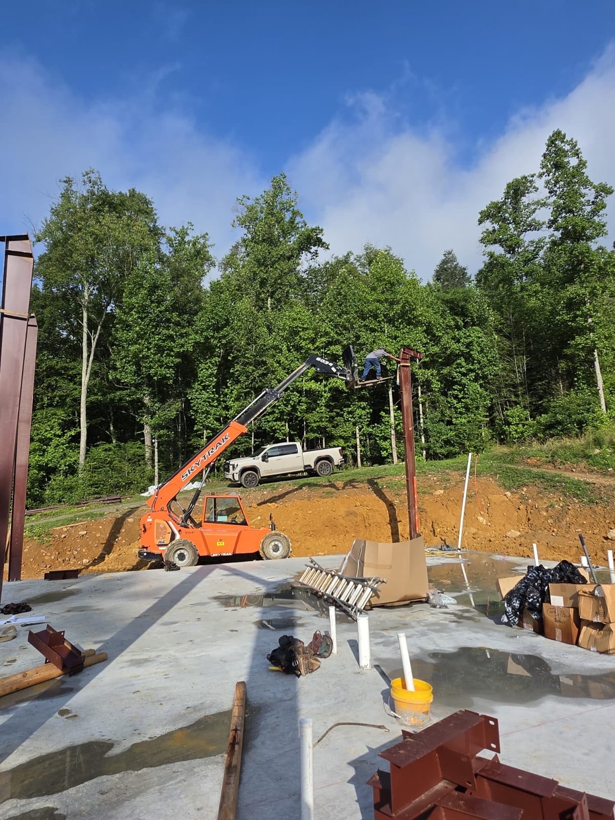 First red-iron column being placed by telehandler on the fresh slab.