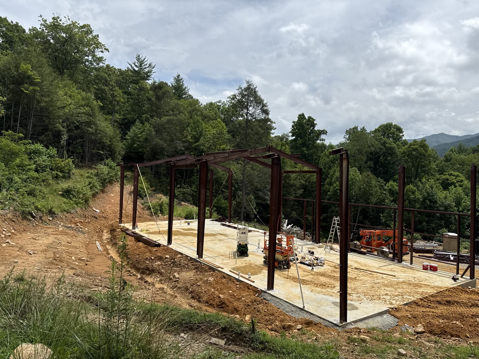 Heavy machinery working alongside the erected frame on the mountain site.