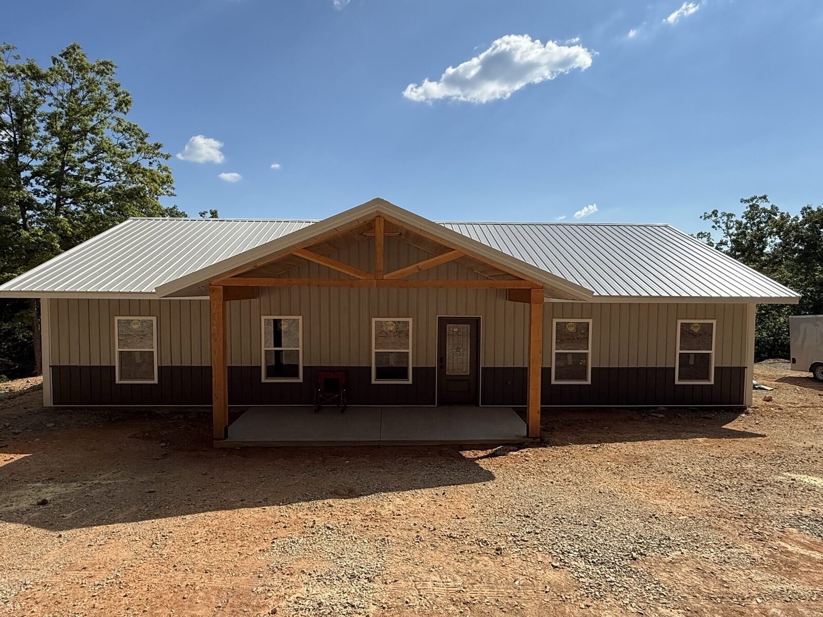 A completed red-iron steel-frame barndominium built by Ozark Closers, straight-on front elevation with cedar-truss porch.
