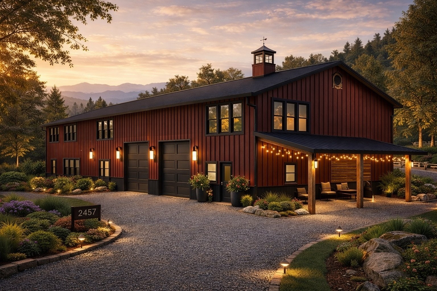 The Truman &mdash; two-story red barndominium with black standing-seam roof, cupola, twin overhead doors, covered side patio with string lights.